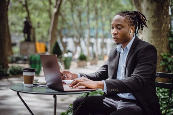 busy young african american man with dreadlocks working on laptop in street cafe