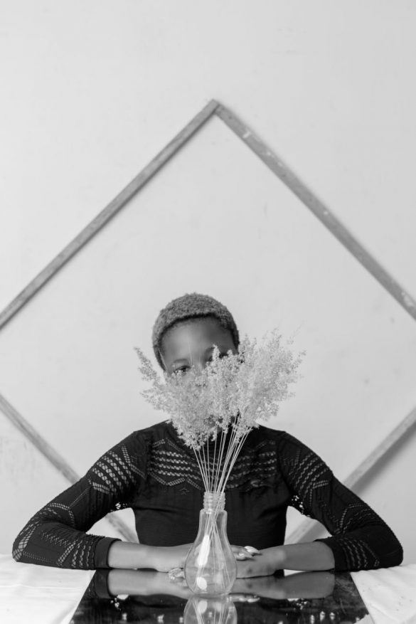 anonymous black woman sitting near flowers vase and window at home